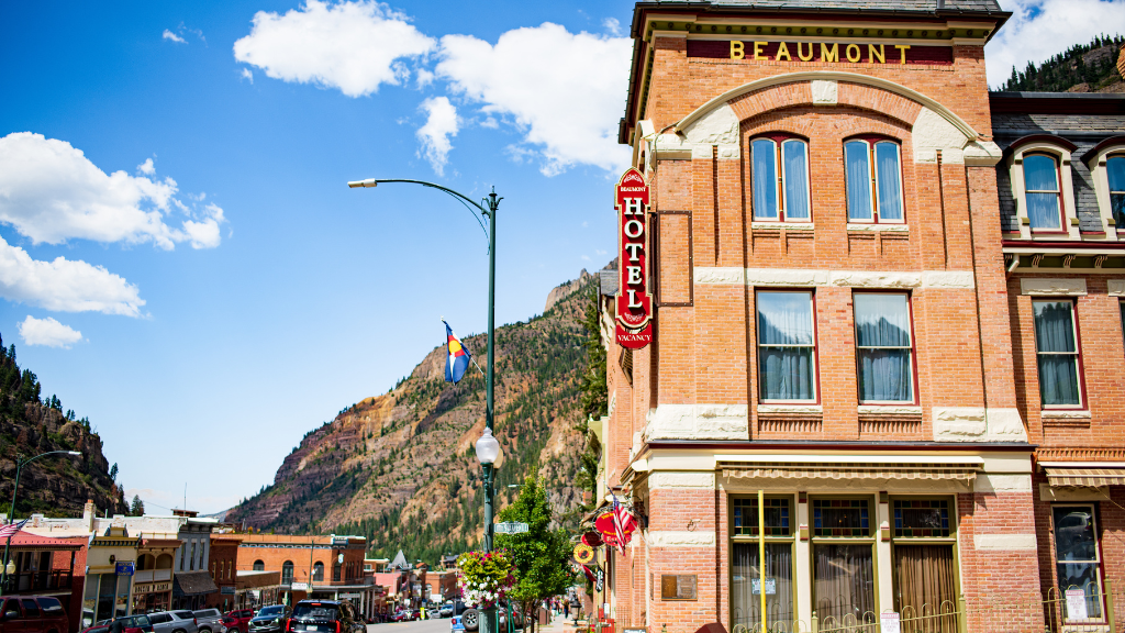 Brick hotel building on a sunny mountain town street with a vertical'HOTEL' sign and blue sky.