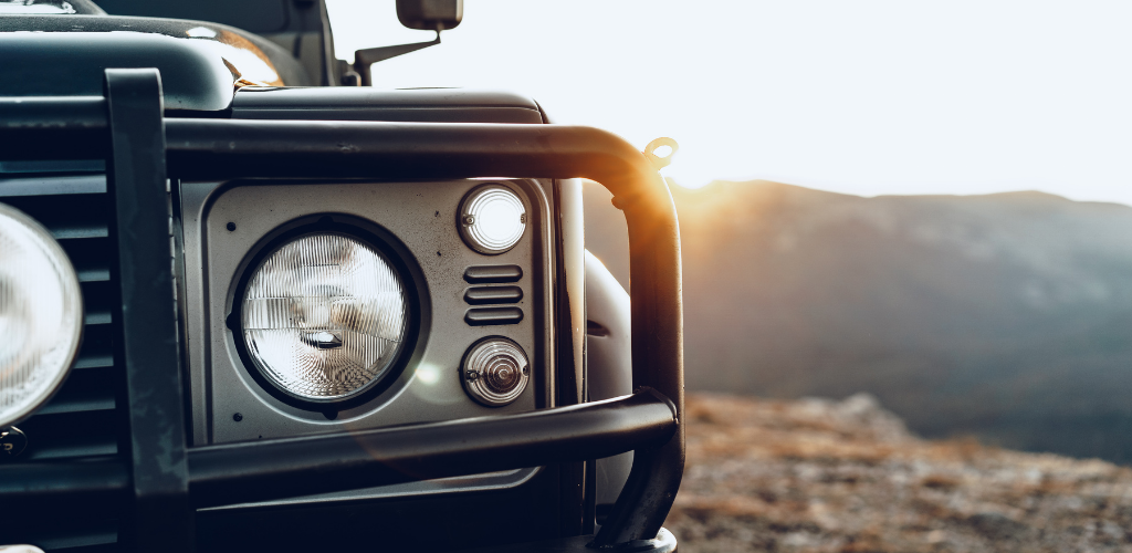Jeep - Beaumont Hotel Front view of a rugged off-road vehicle with a bull bar and large round headlight, sunset in the background.