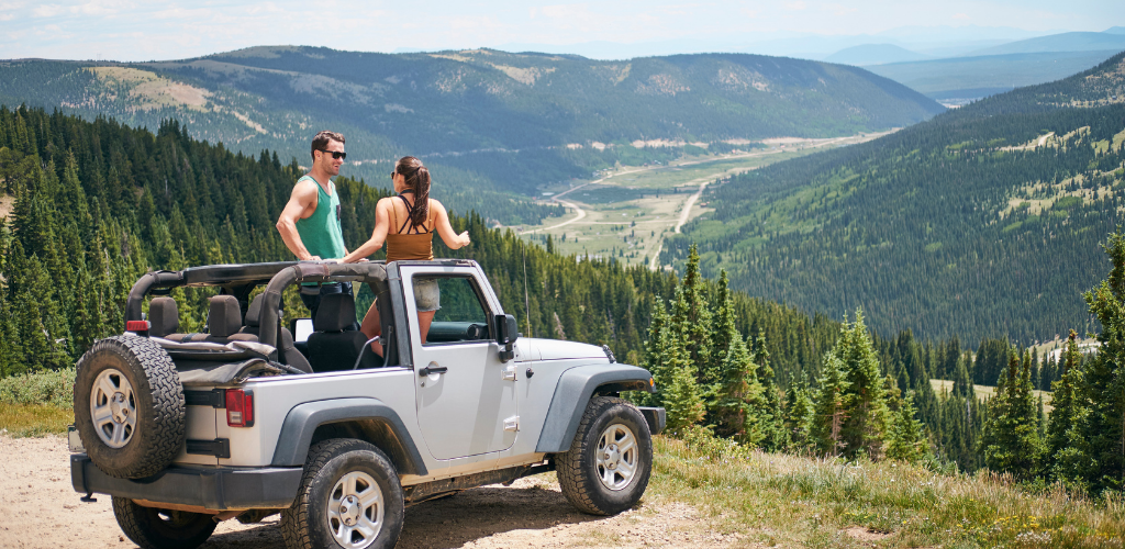 Jeep - Beaumont Hotel Two friends stand beside a white Jeep Wrangler with the top down, overlooking a mountain valley.